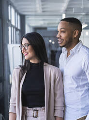 Lächelnde männliche und weibliche Unternehmer, die wegschauen, während sie in einem Coworking-Büro stehen - SNF01256
