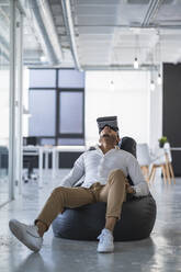 Geschäftsmann benutzt Virtual-Reality-Simulator auf Sitzsack in Coworking-Büro - SNF01257