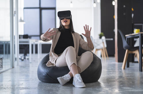 Female professional gesturing while enjoying virtual reality on bean bag in coworking office - SNF01262