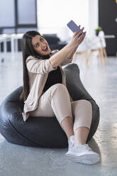 Smiling female entrepreneur taking selfie through mobile phone while sitting on bean bag at office - SNF01264