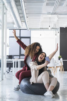 Female entrepreneurs with arms raised having fun while taking selfie through smart phone on bean bag at office - SNF01265