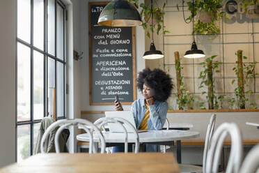 Weibliche Fachkraft mit Hand am Kinn, die ein Smartphone benutzt, während sie in einem Café sitzt - EIF00833