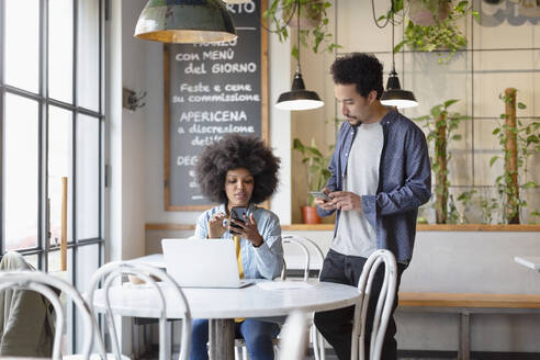 Männliche und weibliche Unternehmer nutzen Smartphones im Café - EIF00842