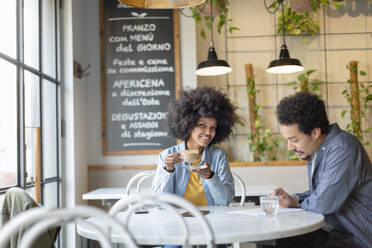 Weibliche Fachkraft trinkt Kaffee, während sie mit einem männlichen Kunden in einem Cafe sitzt - EIF00844