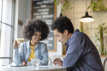 Männlicher Kunde liest Vertrag, während er mit einer Unternehmerin in einem Café sitzt - EIF00846