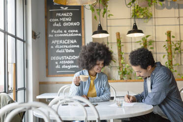 Eine Unternehmerin betrachtet einen männlichen Kunden, der in einem Café einen Vertrag unterzeichnet - EIF00849