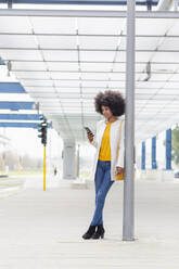Weibliche Fachkraft, die ihr Smartphone benutzt, während sie sich an eine architektonische Säule am Bahnhof lehnt - EIF00863