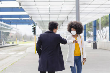 Woman with protective face mask giving elbow bump to male friend at railroad station - EIF00865