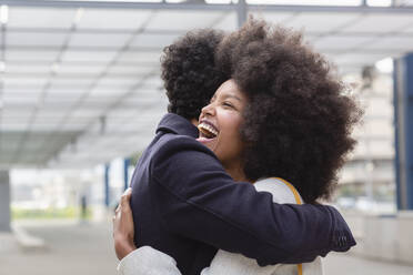 Laughing Afro woman embracing boyfriend at railroad station - EIF00869