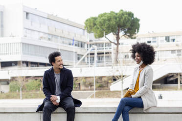 Man and woman following social distancing while sitting on retaining wall - EIF00871