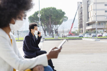 Businessman with protective face mask talking on smart phone following social distancing - EIF00875