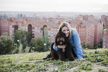 Happy woman embracing Spanish Water Dog in front of cityscape - EBBF03394
