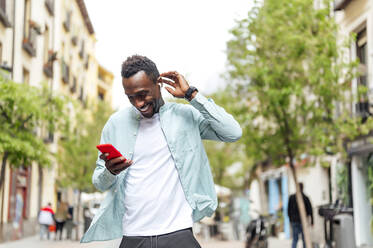 Junger Mann in Freizeitkleidung benutzt sein Smartphone auf der Straße - PGF00535
