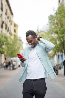 Junger Mann mit Kopf in der Hand, der auf der Straße sein Smartphone benutzt - PGF00536