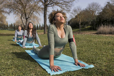 Young women doing upward facing dog position in public park during sunny day - JRVF00464