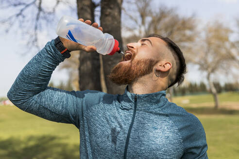 Junger Mann trinkt Wasser in einem öffentlichen Park - JRVF00467