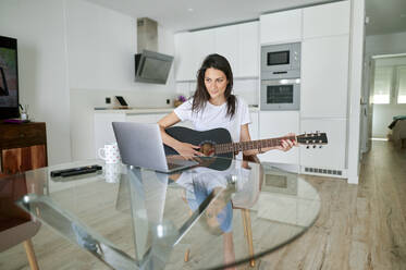 Mid adult woman learning guitar while using laptop at home - KIJF03790