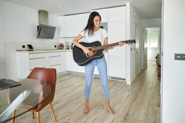 Smiling woman playing guitar at home - KIJF03792