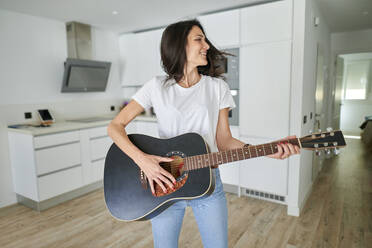 Glückliche Frau spielt Gitarre zu Hause - KIJF03793