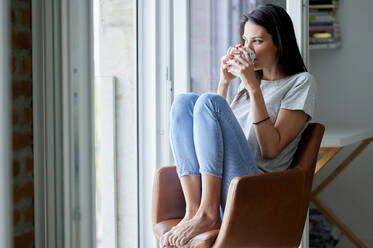Nachdenkliche Frau schaut weg, während sie zu Hause Kaffee trinkt - KIJF03805