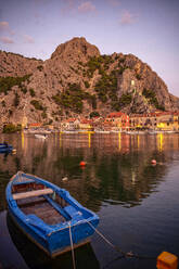 Kroatien, Gespanschaft Split-Dalmatien, Omis, Ruderboot vor der Küstenstadt in der Abenddämmerung vertäut - MAMF01727
