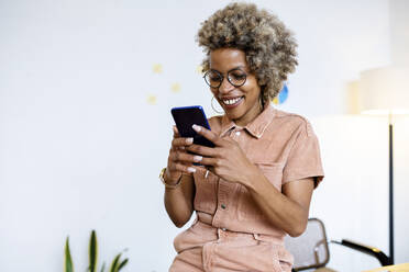 Smiling female entrepreneur using smart phone at home office - RFTF00053