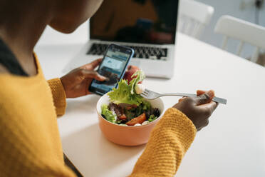 Junge Frau frühstückt gesund, während sie zu Hause ihr Smartphone benutzt - MPPF01668