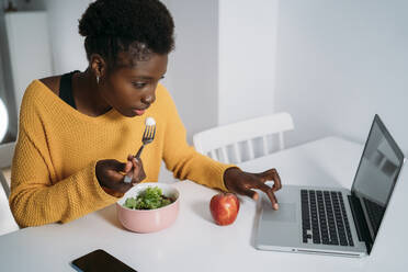 Female entrepreneur having breakfast while using laptop at table - MPPF01670
