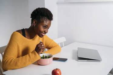 Happy young woman having healthy breakfast at table while looking away - MPPF01671