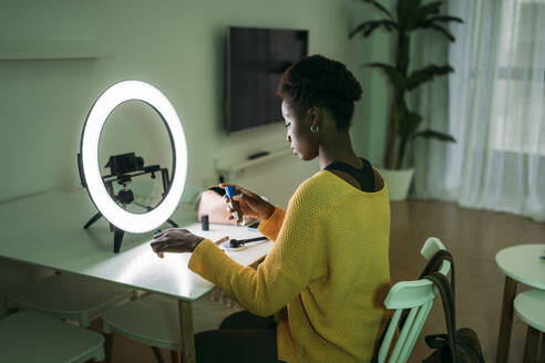 Female influencer in front of illuminated ring light while vlogging at home - MPPF01679