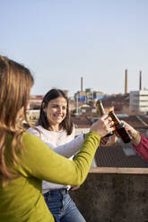 Female friends toasting beer bottles on rooftop - VEGF04273