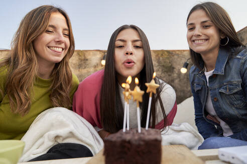 Junge Frau mit Freundinnen bläst an ihrem Geburtstag Kerzen aus - VEGF04285