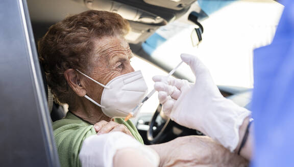 Ältere Frau wird von einer Ärztin im Auto geimpft - JCCMF01985