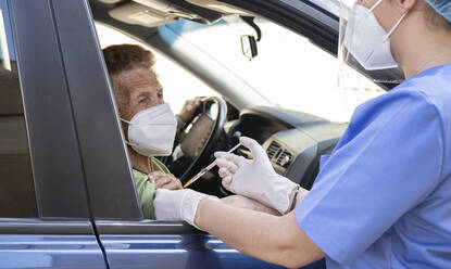 Senior woman getting COVID-19 vaccine from female doctor at drive through - JCCMF01988