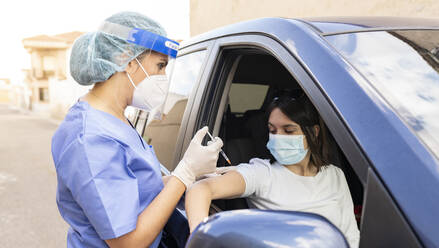 Mittlere erwachsene Frau wird im Auto von einer Ärztin geimpft - JCCMF01993