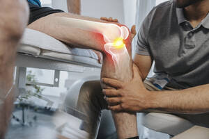 Physiotherapeutin überprüft das Kniegelenk eines Patienten im medizinischen Untersuchungsraum - LIFIF00025