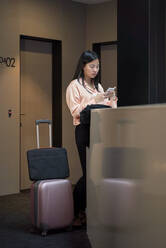 Eine Unternehmerin benutzt ein Smartphone, während sie im Korridor eines Hotels steht - VEGF04294