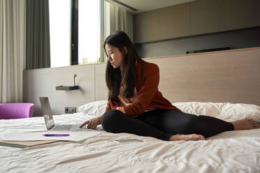 Female entrepreneur using laptop on bed in hotel - VEGF04305