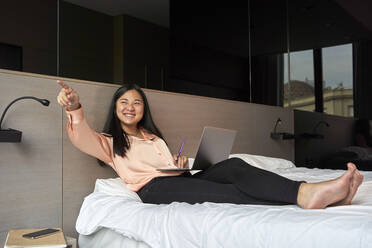 Lächelnde weibliche Fachkraft, die mit einem Laptop im Hotel sitzt und darauf zeigt - VEGF04314