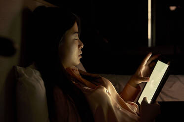 Businesswoman using digital tablet in dark at hotel - VEGF04320