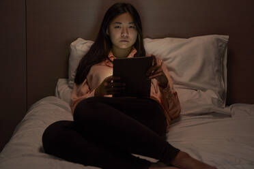 Junge Geschäftsfrau mit digitalem Tablet auf dem Bett im Hotel sitzend - VEGF04321