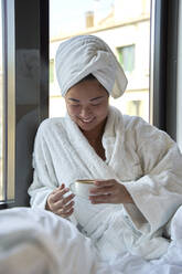 Smiling woman holding coffee cup in hotel - VEGF04327