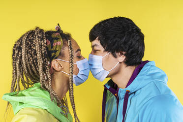 Couple with face mask kissing each other by yellow background - OIPF00493