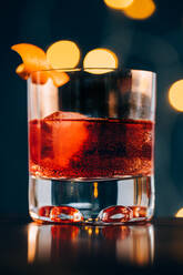 Ein Glas mit einem erfrischenden alkoholischen Negroni-Cocktail, garniert mit einer reifen Orangenschale, wird auf den Tisch gestellt, inmitten der Werkzeuge des Barkeepers - ADSF23134