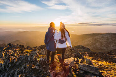 Rückenansicht eines anonymen Touristenpaares, das die majestätischen Berge unter einem strahlenden Himmel im Sonnenlicht bewundert - ADSF23143