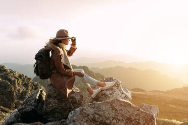 Seitenansicht eines nicht erkennbaren Wanderers, der auf einem Stein sitzt und die herrliche Landschaft des Hochtals an einem sonnigen Tag betrachtet - ADSF23161