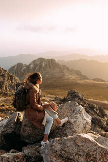 Seitenansicht eines nicht erkennbaren Wanderers, der auf einem Stein sitzt und die herrliche Landschaft des Hochtals an einem sonnigen Tag betrachtet - ADSF23162