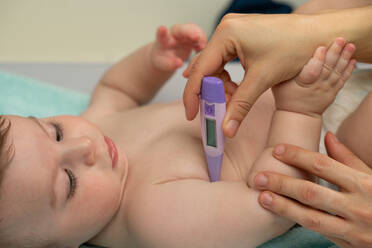 Crop liebende Mutter Messung der Temperatur der niedlichen Baby und Platzierung Thermometer in Baby Achselhöhle sorgfältig - ADSF23169