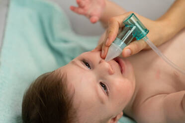 Pflegende Mutter, die eine Saugmaschine in das Nasenloch des Babys einführt, um den Schleim zu entfernen - ADSF23170