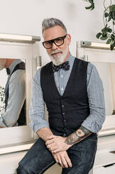 Trendy reifen Hipster Geschäftsmann in Brillen und trendige Kleidung Blick auf Kamera auf Stuhl im Haus - ADSF23180